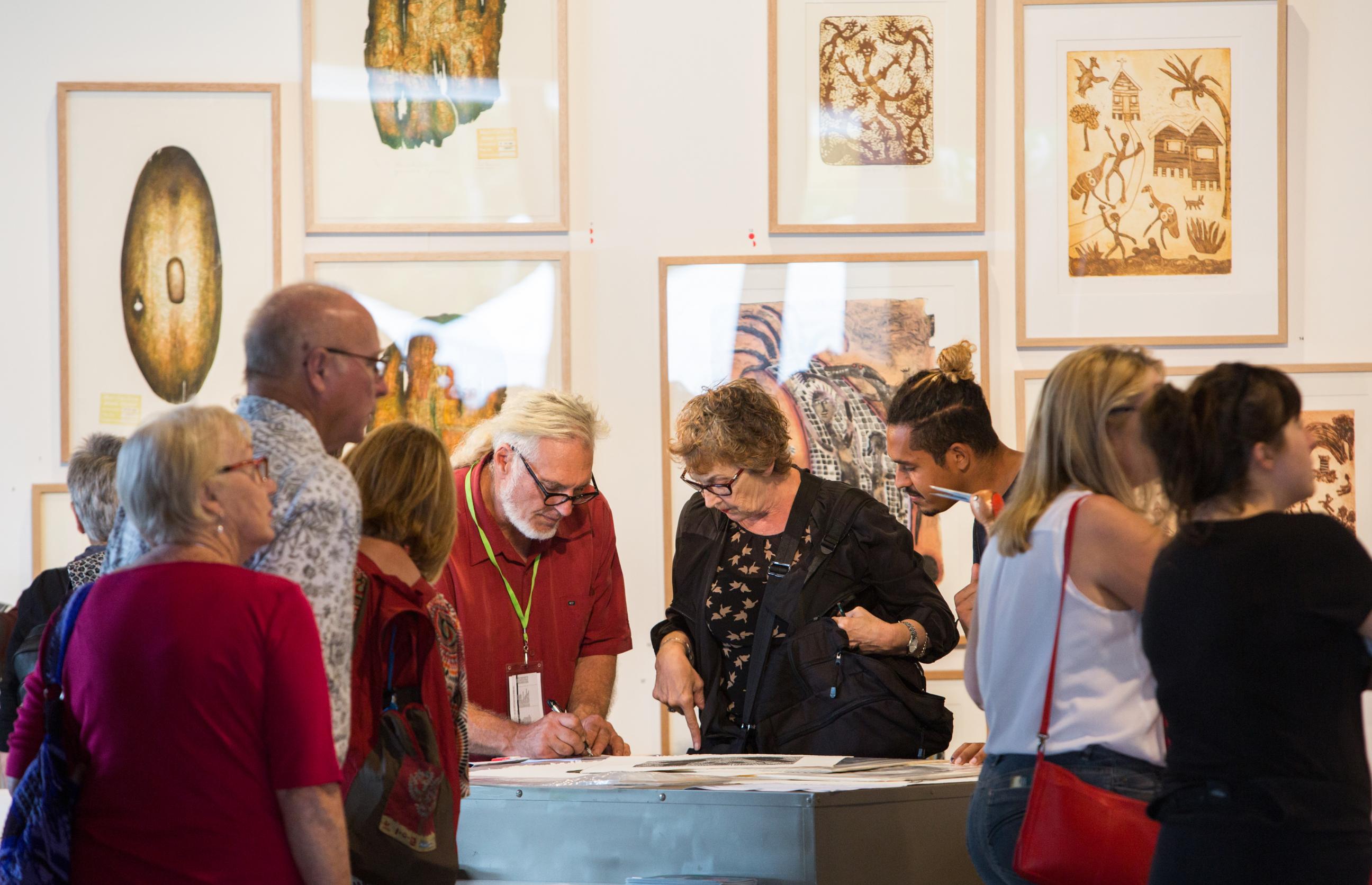A group of people wearing casual clothes looking at a table of artwork at the Cairns Indigenous Art Fair